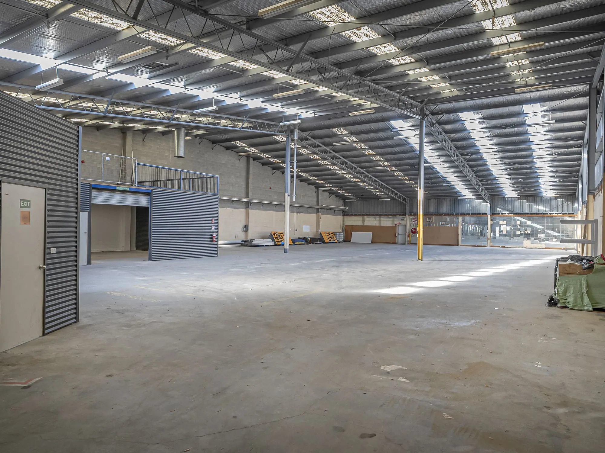 Warehouse interior with an enclosed area under a mezzanine platform, roller shutter and exit door.