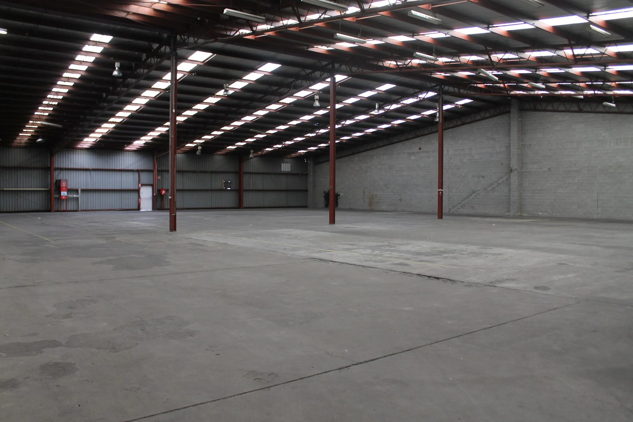 Further warehouse area with red painted steel columns, blockwork side wall and bare concrete floor.