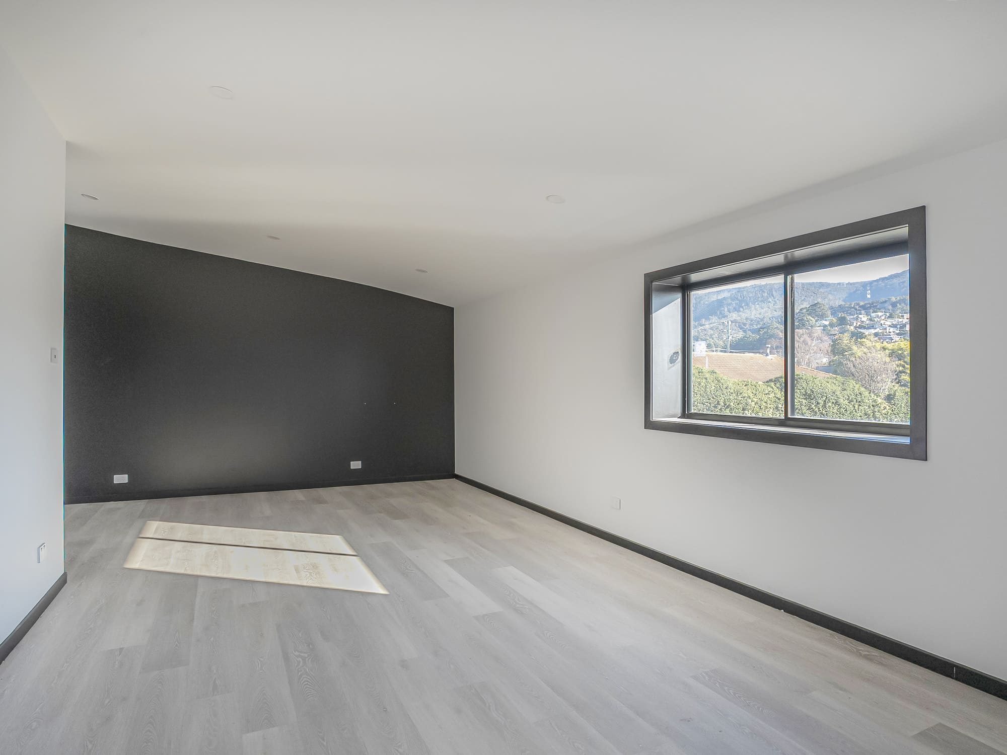 Empty office room with timber-look flooring, a dark feature wall and a window looking towards the hills.